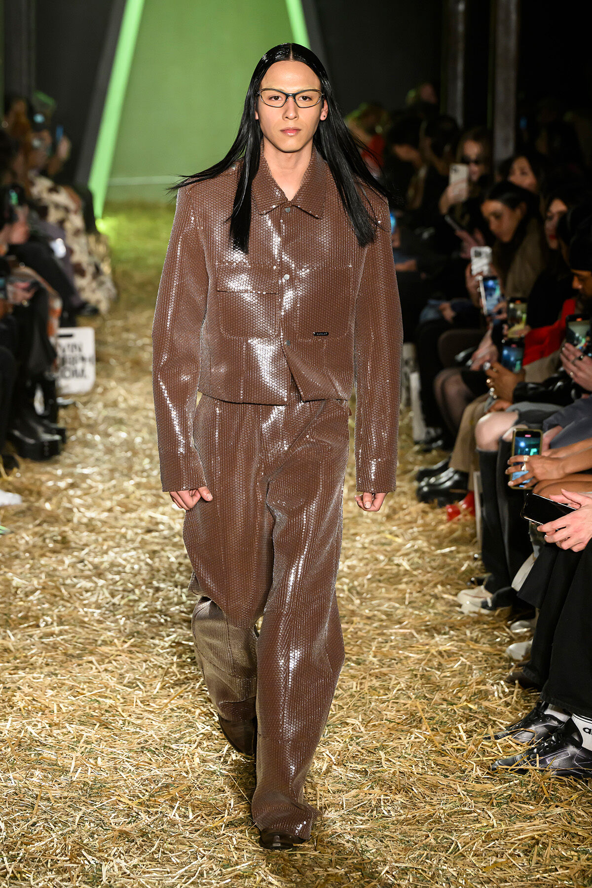 Model walking the runway in a glossy brown suit at NYFW F/W 2024.